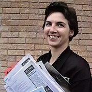 Smiling woman with short dark hair holding an armful of papers and other items